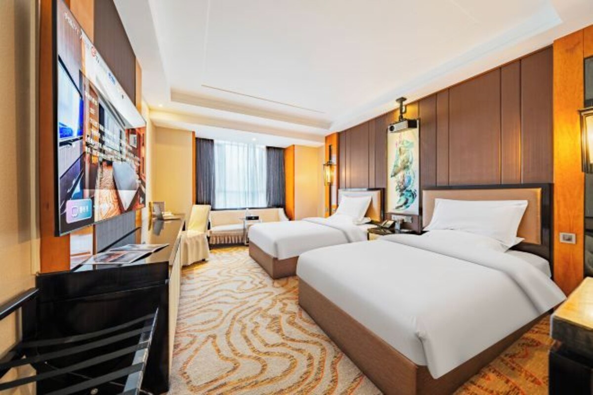 Ein Hotelzimmer mit zwei Betten, einem Schreibtisch, einem Stuhl, einem Fernseher und einem großen Fenster.