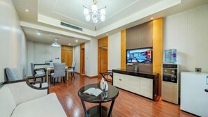 Una habitación de hotel moderna con comedor, cocina, sala de estar con sofá y mesa de centro, y televisión.
