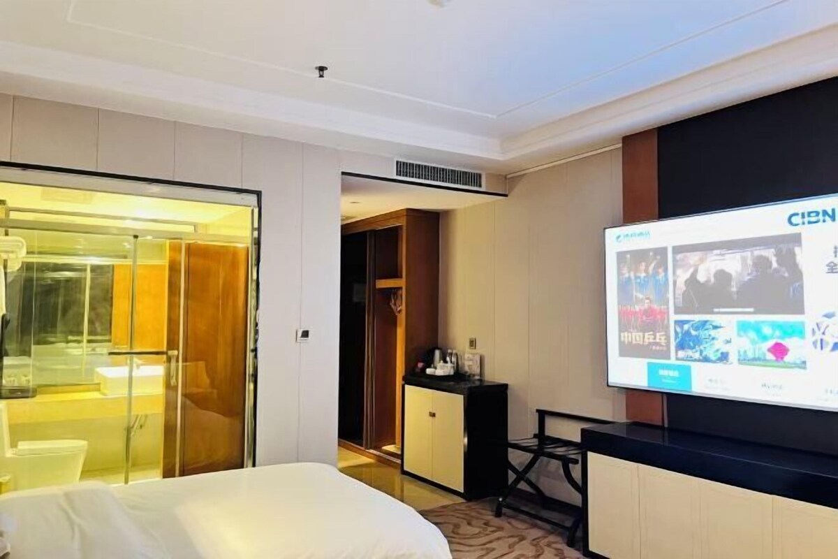 A hotel room with a bed, a TV screen displaying a movie, a wardrobe, and a desk with a chair.