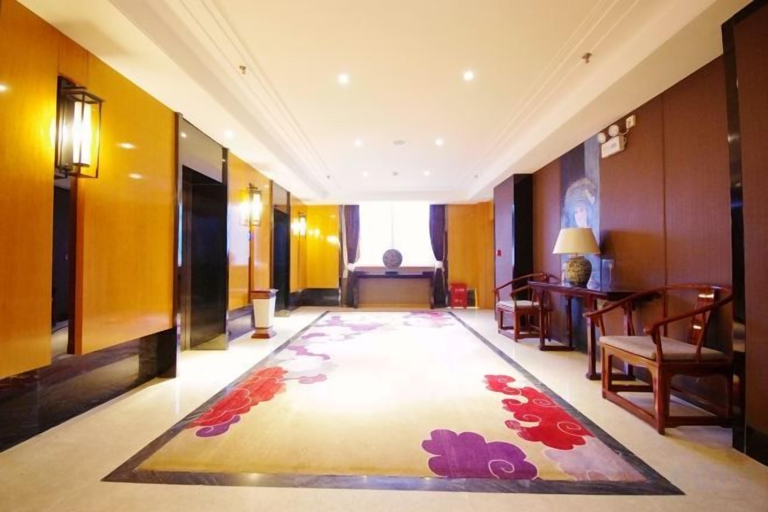 Een hotel lobby met een lange receptiebalie, een zithoek en een vloerkleed met bloemenmotieven.