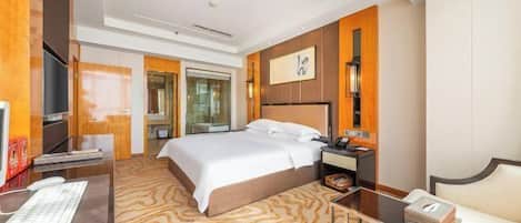 A hotel room with a large bed, a desk with a computer, a bedside table with a lamp, and a TV.