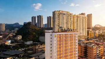 Un edificio de gran altura con varios pisos, rodeado de otros edificios y un paisaje montañoso al fondo.