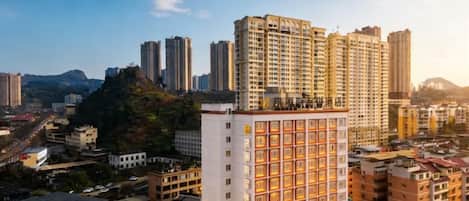 A high-rise building with multiple floors, surrounded by other buildings and a hilly landscape in the background.