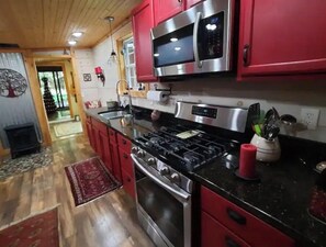 Une cuisine avec des meubles de couleur rouge, des appareils en acier inoxydable et un plan de travail noir.