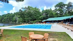 En swimmingpool med liggestole og et bord i forgrunden, omgivet af et træhegn.