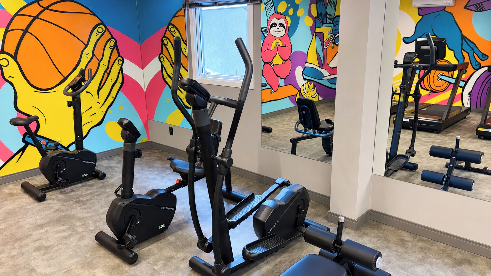 A gym with stationary bikes, a treadmill, and a mirror reflecting the equipment.