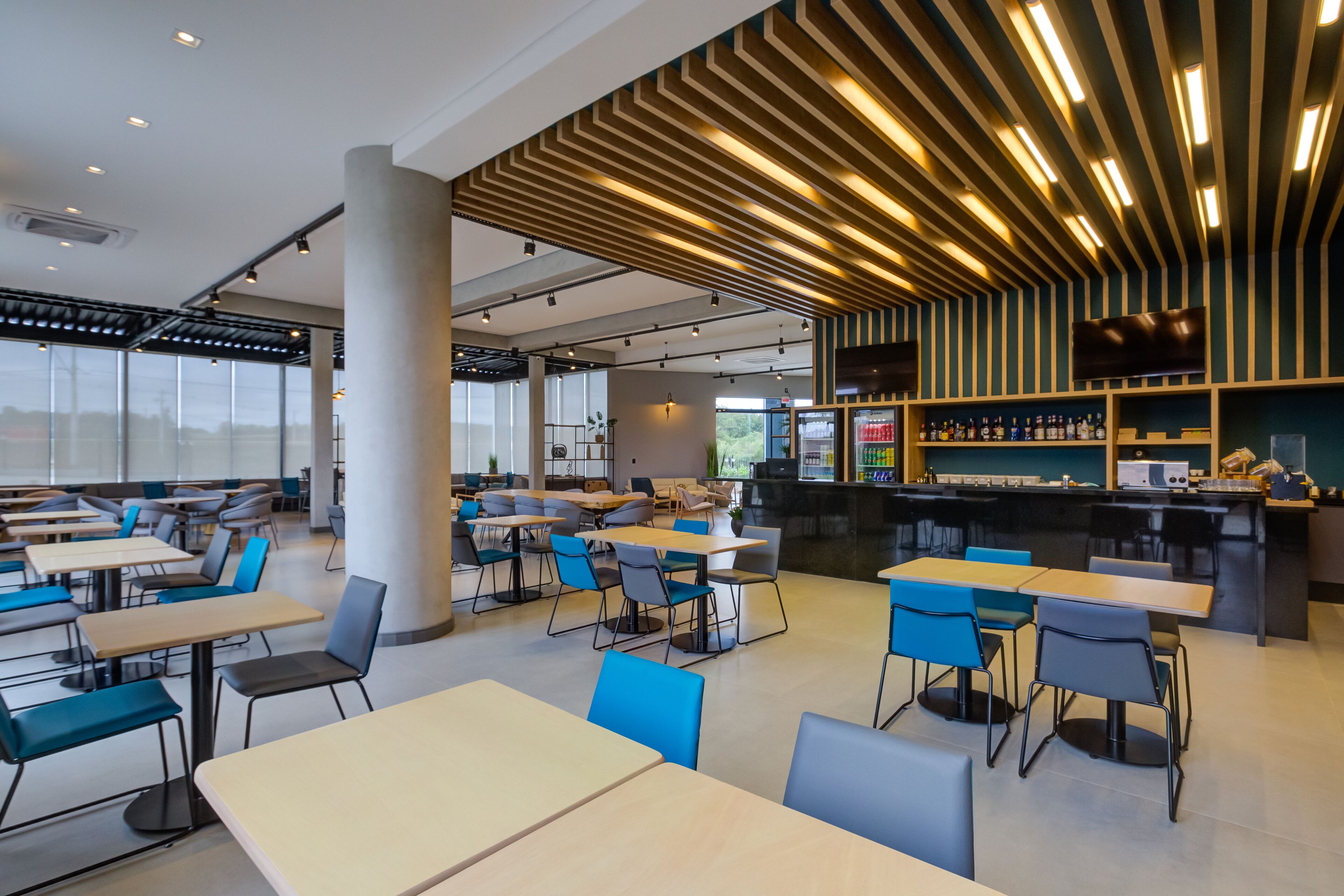 Un restaurante moderno con varias mesas y sillas, una zona de bar y grandes ventanales.