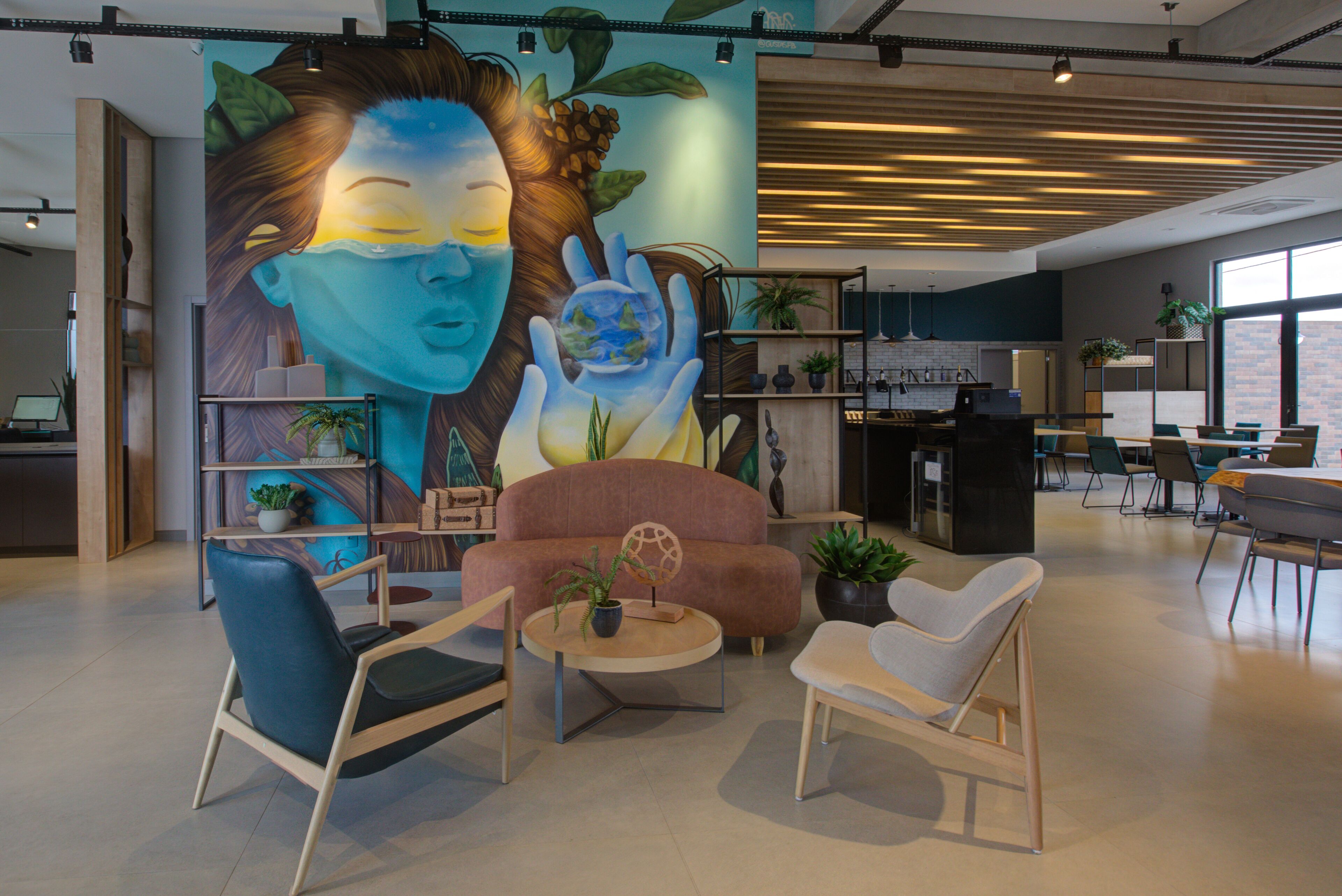 Un área de estar moderna con un mural, asientos cómodos y una cocina al fondo.