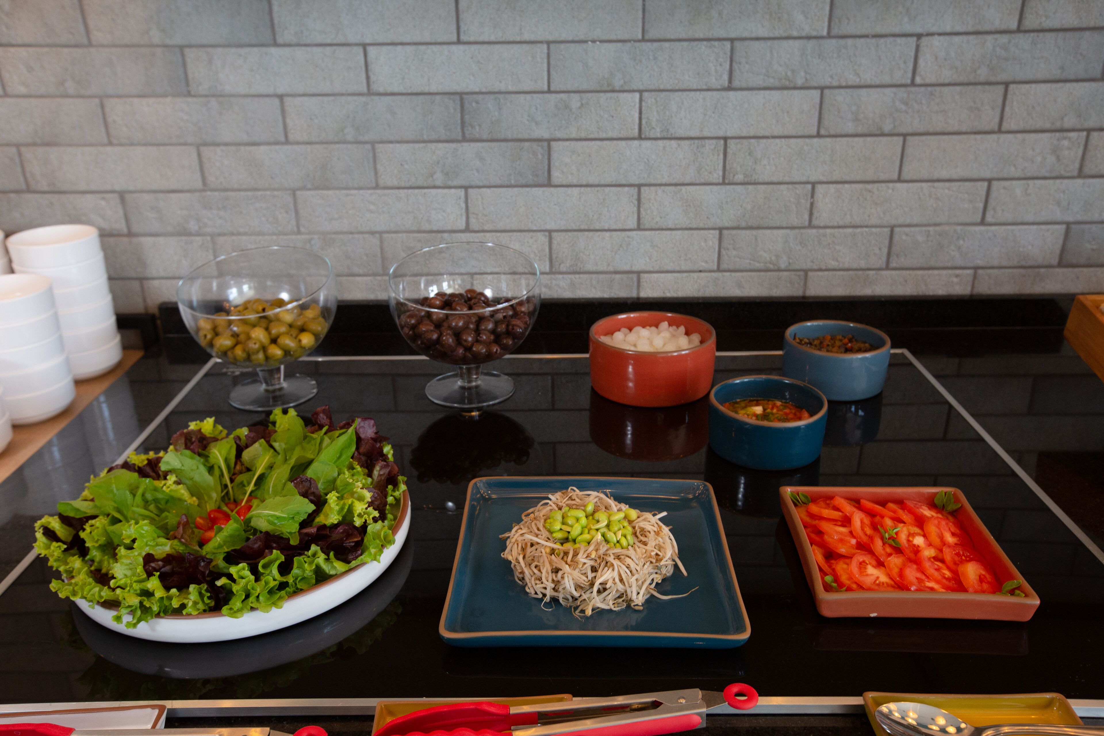 A table with various food items and condiments, including a salad, noodles, and sliced tomatoes.