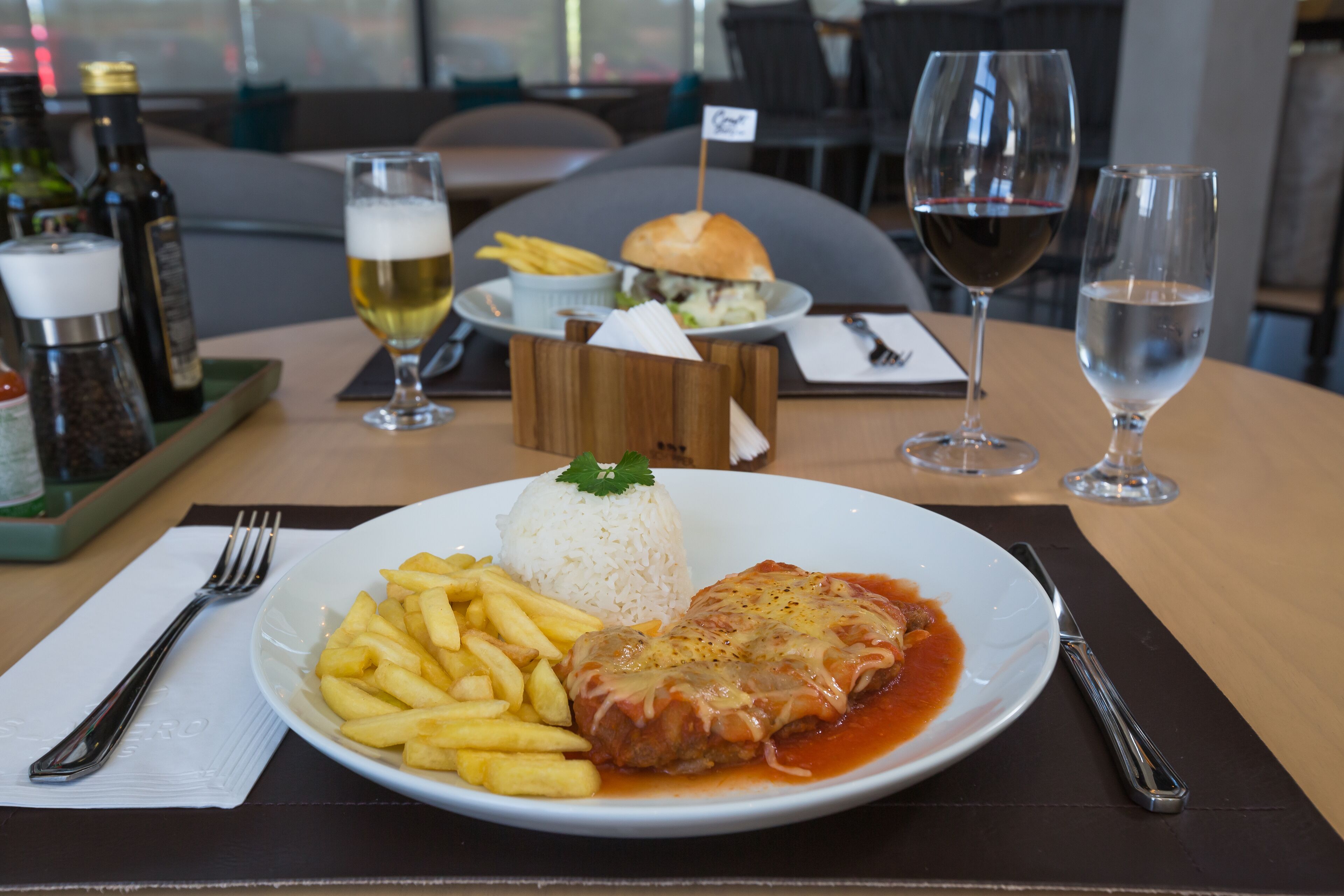 A dining table with a plate of food, including a fish fillet, rice, and fries, and two glasses of wine.