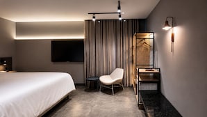Una habitación de hotel moderna con una cama grande, una silla, una mesita, un televisor y una lámpara de pared de diseño único.