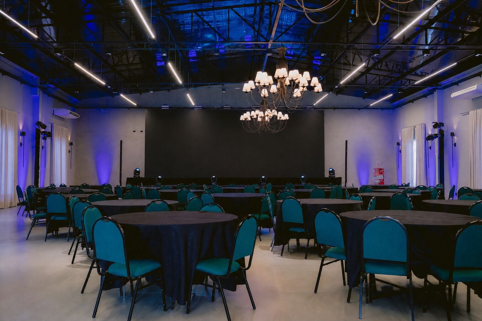 Un salón de conferencias con varias mesas y sillas, una pantalla grande y una lámpara de araña.