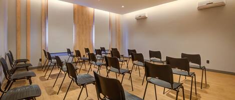 Un salón de conferencias con filas de sillas negras, paneles de madera y luces empotradas en el techo.