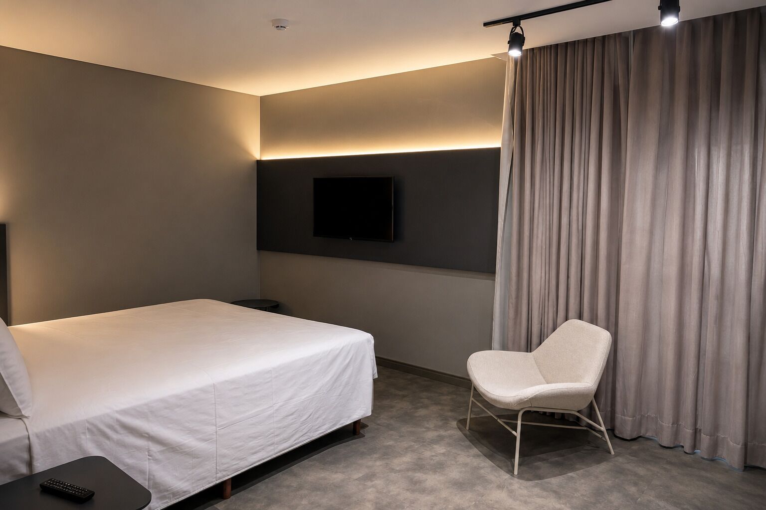 Habitación de hotel con cama, una silla, televisor montado en la pared y cortina.