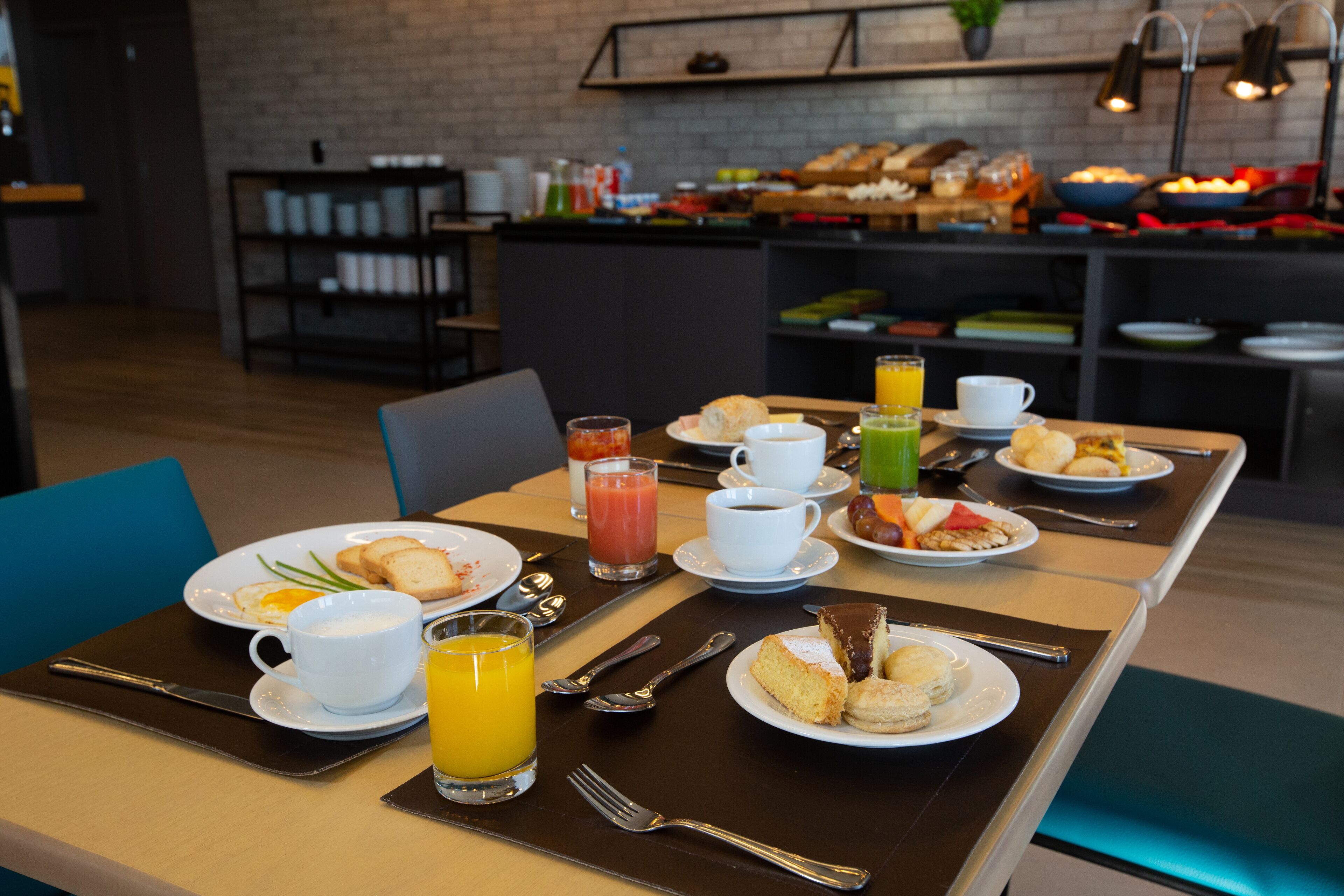 A breakfast setting with a variety of food items and beverages on a table, including plates with eggs, toast, and pastries, along with cups of coffee and orange juice.