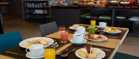 A breakfast setting with a variety of food items and beverages on a table, including plates with eggs, toast, and pastries, along with cups of coffee and orange juice.