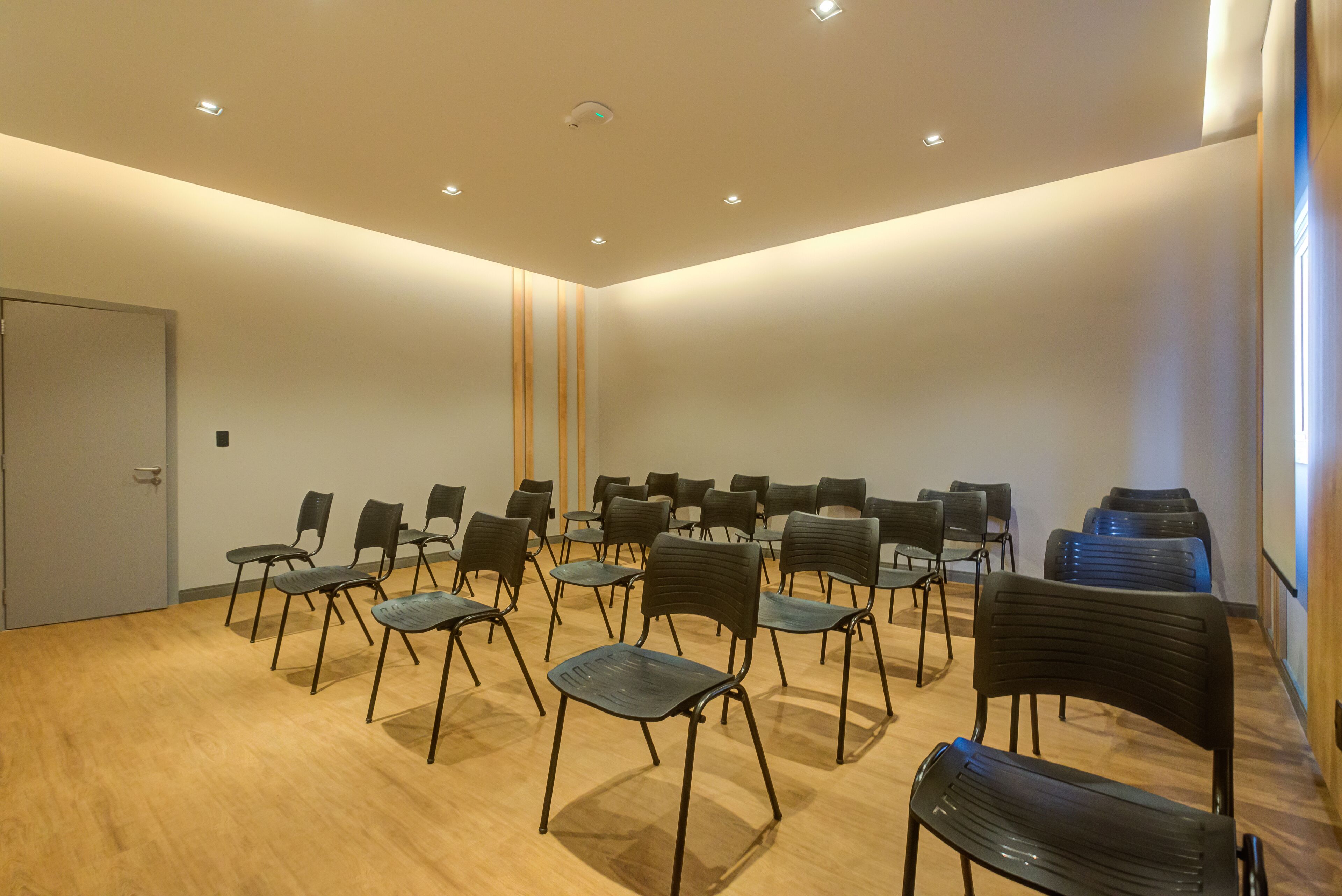 Una sala conferenze con file di sedie, un pavimento in legno e una porta a sinistra.
