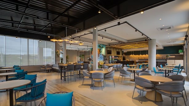 Un espacio interior amplio con diversas disposiciones de asientos, incluyendo mesas redondas y sillas, y una zona de cocina al fondo.