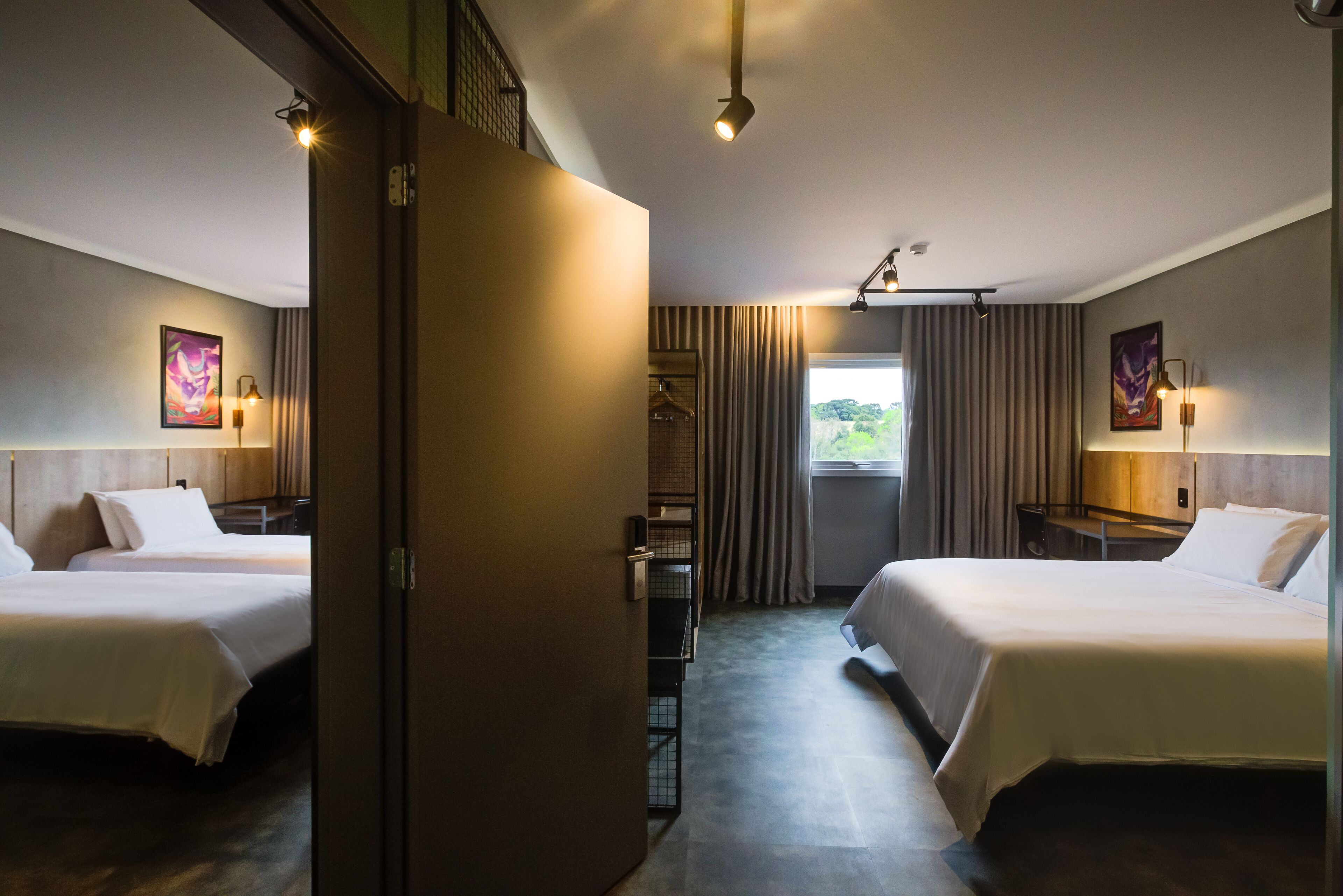 A hotel room with two beds, a wardrobe, a desk with a lamp, and a window with curtains.