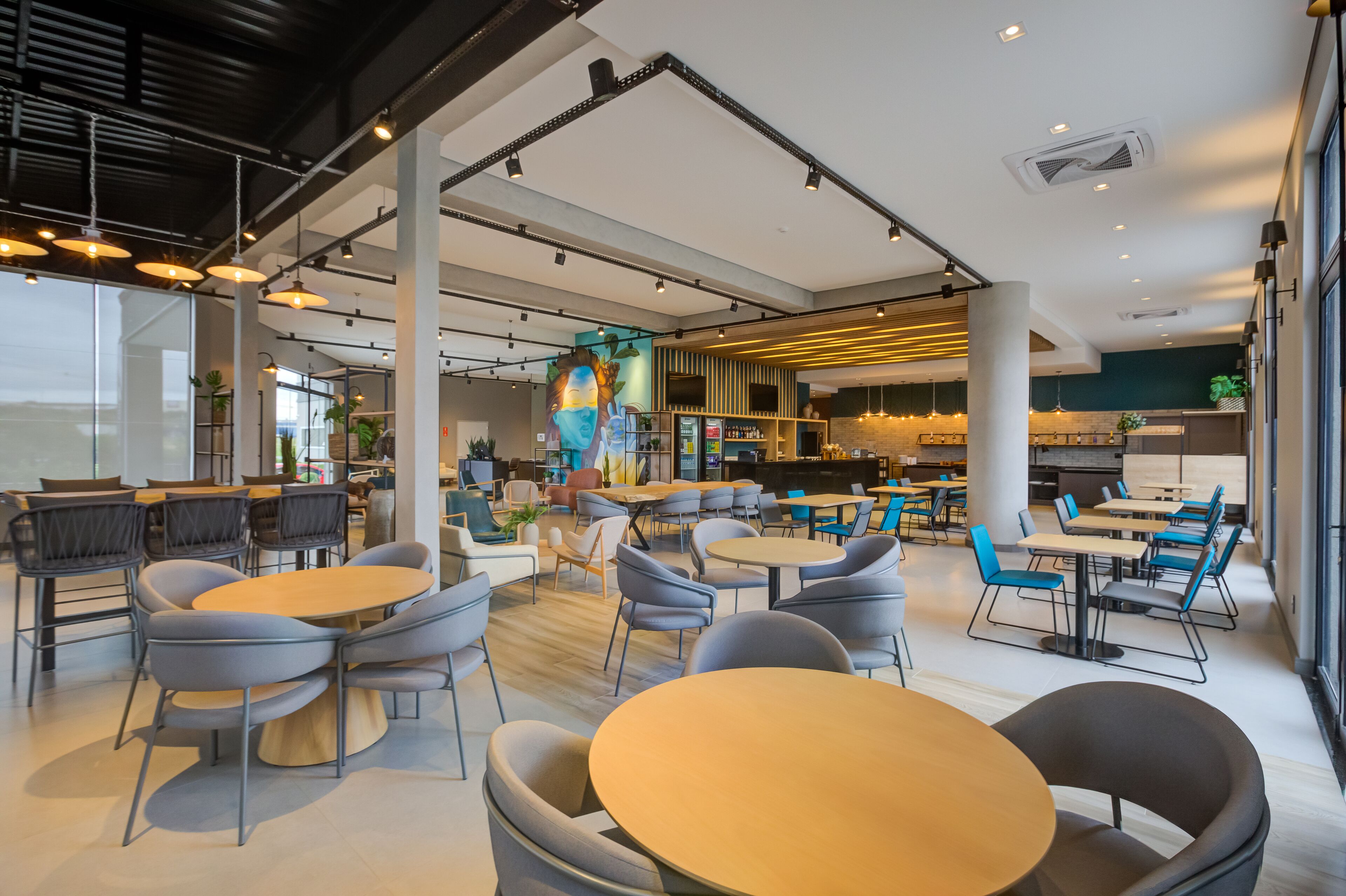 Un café moderno con mesas y sillas redondas, una zona de bar y ventanas amplias.