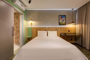 Habitación de hotel con una cama grande, un escritorio, una silla, una lámpara y un cuadro en la pared.