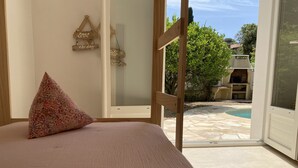 Ein Schlafzimmer mit einem Bett, einem Zierkissen und Blick auf einen Außenpool durch eine Glastür.