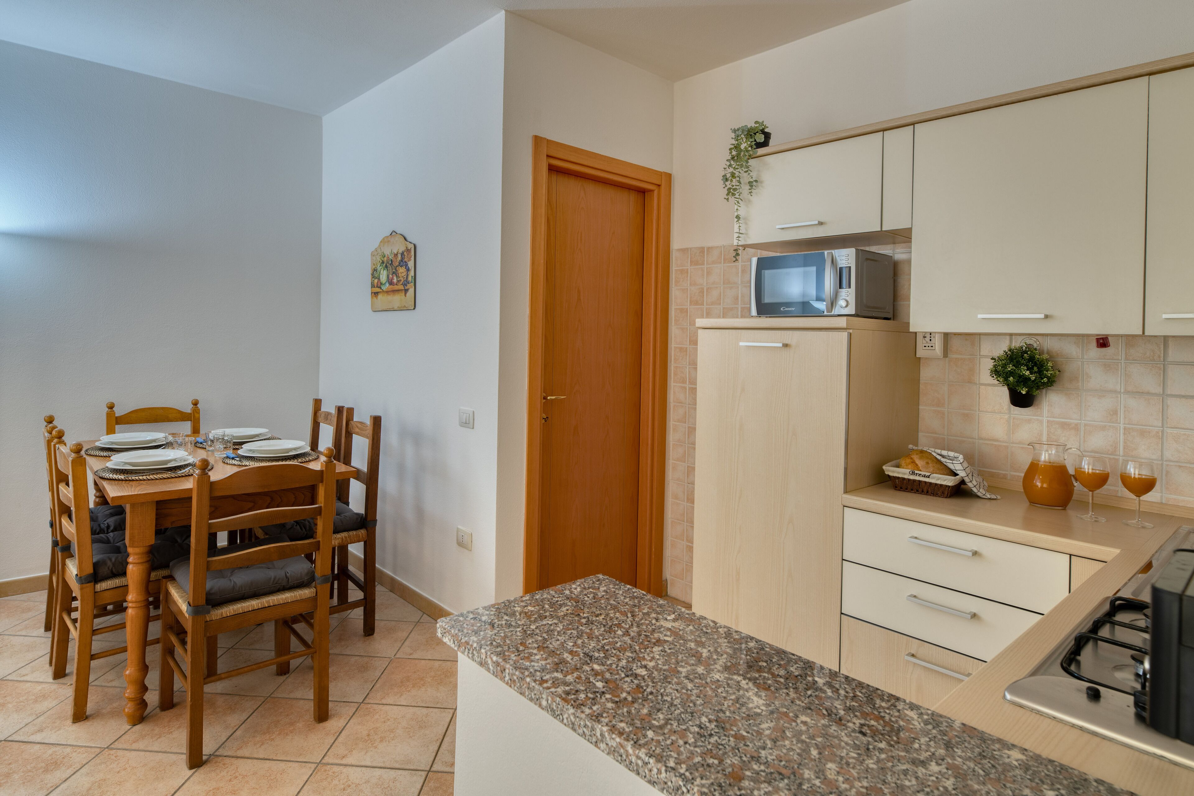 A kitchen with a granite countertop, wooden cabinets, a microwave, and a dining area with a wooden table and chairs.