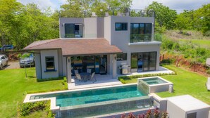 A modern two-story house with a large glass front, a swimming pool, and a patio area.