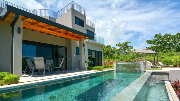 A modern two-story house with a swimming pool, outdoor seating, and a covered patio.