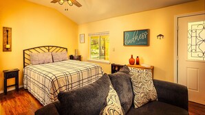 Une chambre à coucher avec un lit, un ventilateur de plafond, une fenêtre, un mur avec une affiche et une porte.