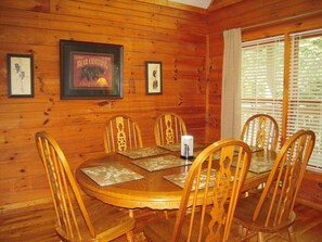 Enjoy meals in this cozy dining area with a wooden table and chairs, framed pictures on the wall, and a window with blinds.