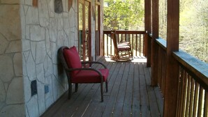 A wooden deck with a stone wall, a red chair, and a rocking chair. - Countryside in Country Pines (Sevierville)