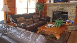 A cozy living room with leather sofas, a stone fireplace, and a television mounted above it. - Countryside in Country Pines (Sevierville)