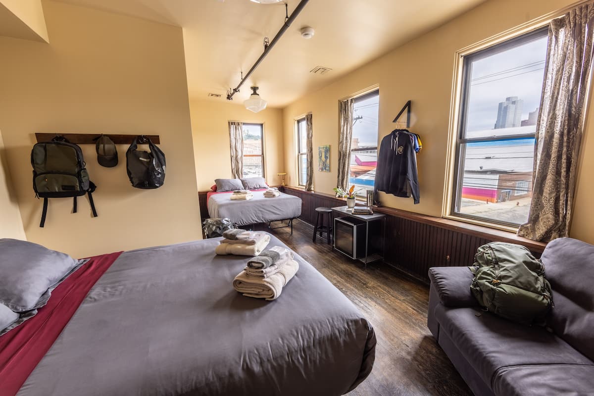A hotel room with two beds, a sofa, a desk, and a view of the city.