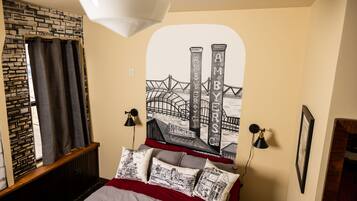 A bedroom with a bed, a wall-mounted lamp, a framed picture, and a window with curtains.