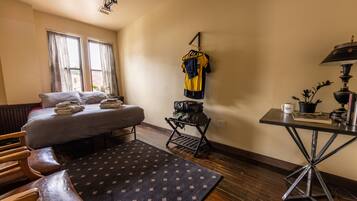 Quarto de hotel com cama, escrivaninha, cadeira, tapete e uma camisola pendurada na parede.