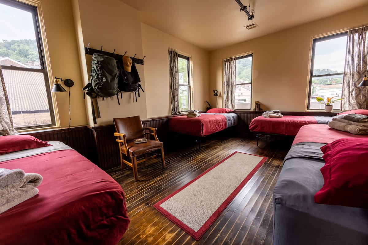 A hotel room with three beds, wooden flooring, and large windows.