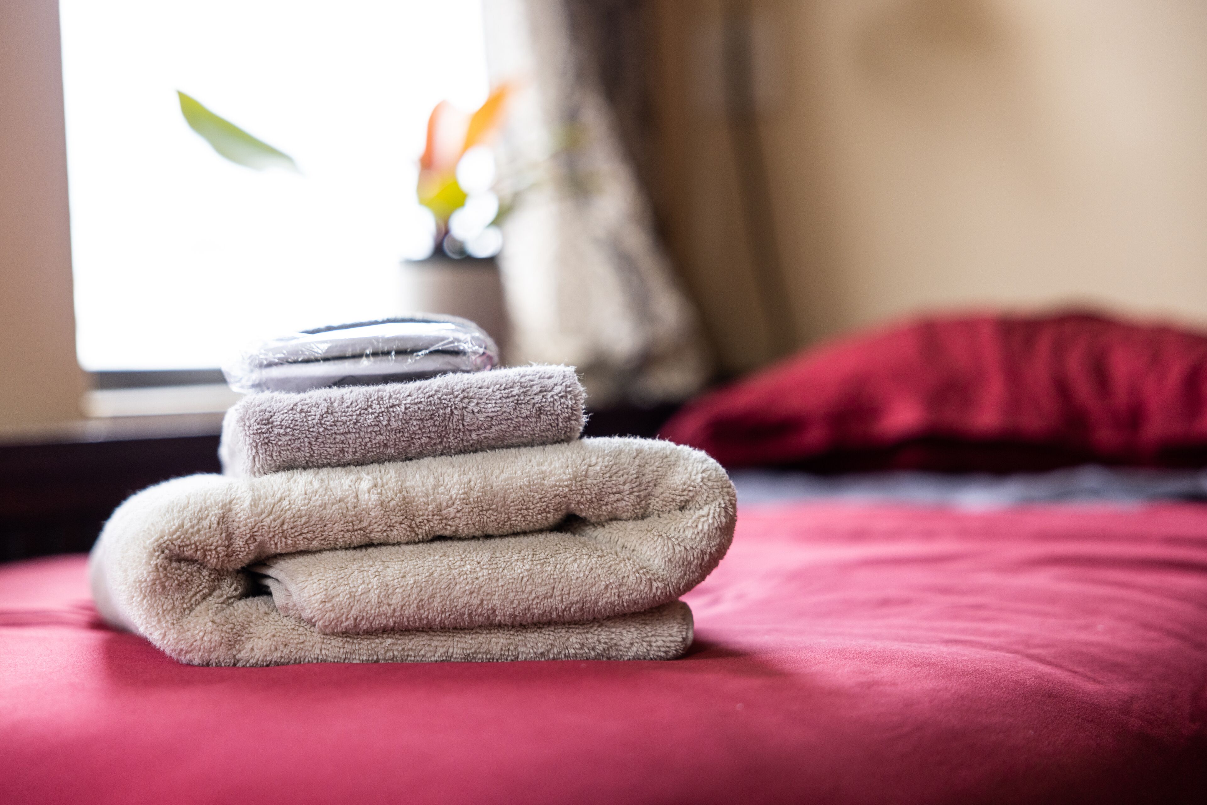 Un montón de toallas dobladas sobre una cama con cubrecolor rojo.
