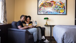 A room with a sofa, a bed, a framed painting, a lamp, and a window with curtains. - Traveler's Rest Hotel (Pittsburgh)