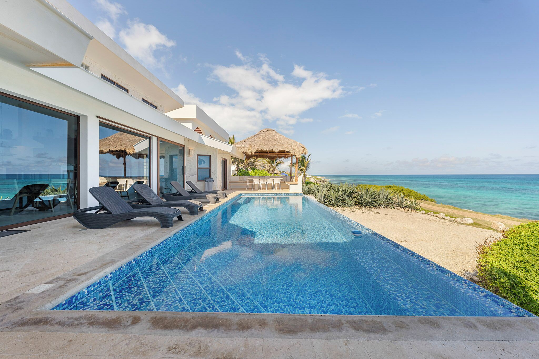 Une piscine moderne avec une eau d’un bleu cristallin, des chaises longues et une vue sur l’océan.