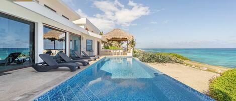 A modern pool with clear blue water, lounge chairs, and a view of the ocean.