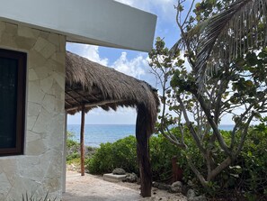 Un bâtiment en pierre avec un toit de chaume, une vue sur la mer et une végétation luxuriante tout autour.