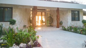 A modern building with a stone facade, a covered entrance, and a garden with various plants and flowers.