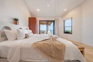 Een slaapkamer met een groot bed, een potplant, een houten bank en uitzicht op de omgeving.