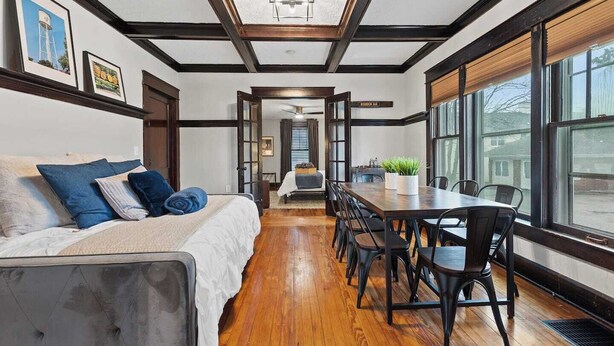 A modern interior with a wooden dining table, chairs, a sofa with blue cushions, and a large window offering a view of the outside. - This gem sits in the heart of picturesque South Frankfort, near the Kentucky river (Frankfort)