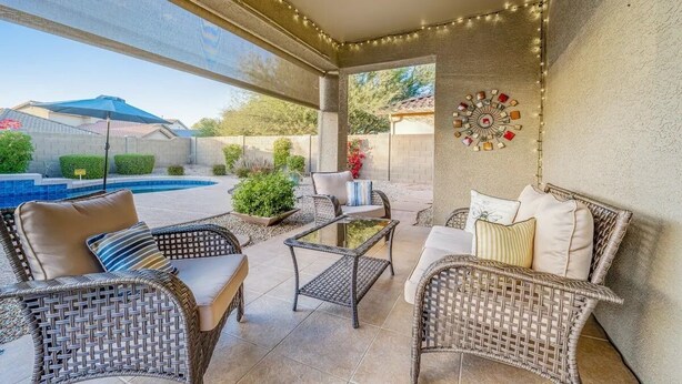 An outdoor patio with wicker furniture, a glass table, and string lights. - NEW! Cozy desert getaway with private backyard and seasonal pool! (New River)