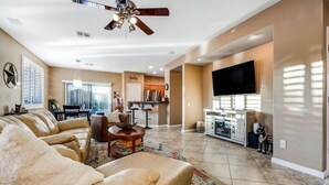 A spacious living room with a large sectional sofa, a ceiling fan, a flat-screen TV, and a kitchen area with modern appliances. - NEW! Cozy desert getaway with private backyard and seasonal pool! (New River)