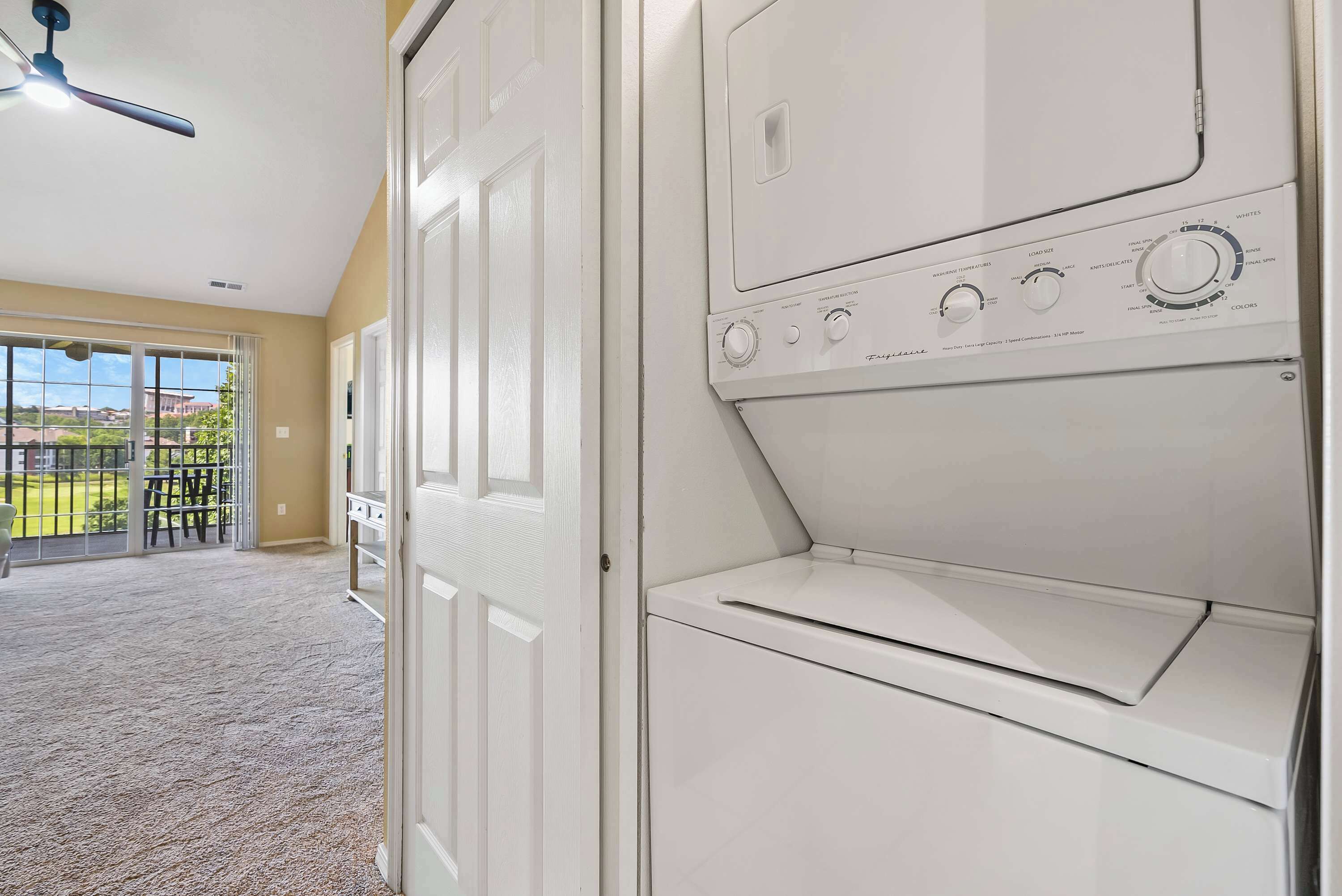 A laundry room with a front-loading washer and dryer, a ceiling fan, and a view of a balcony with outdoor furniture.