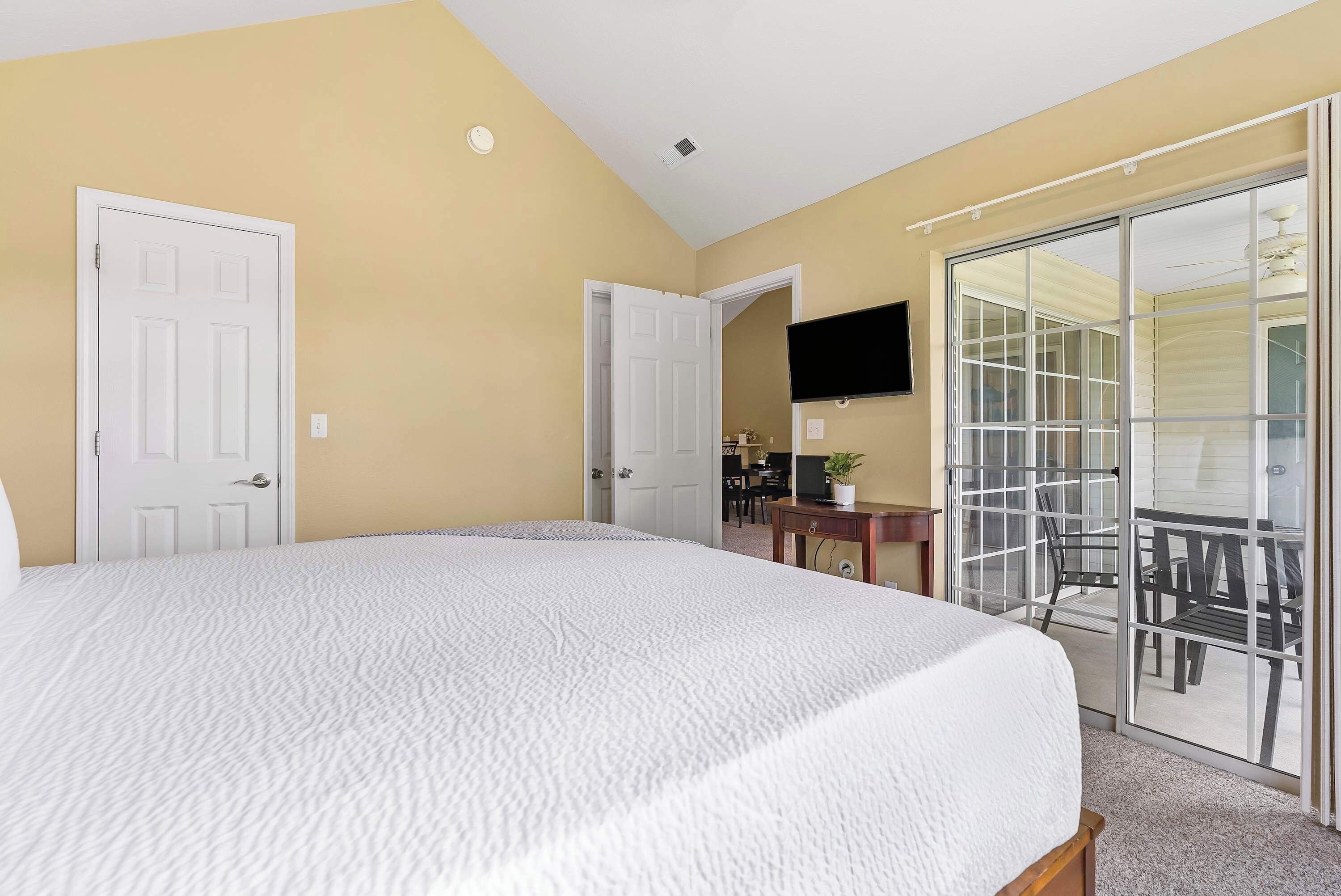 A bedroom with a large bed, a sliding glass door to a balcony, and a flat-screen TV mounted on the wall.