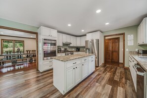 A spacious kitchen with white cabinetry, a central island, and a dining area with a long table and chairs. - Deer Run Manor - Indoor Pool, Hot Tub & Game Room (Rockbridge)